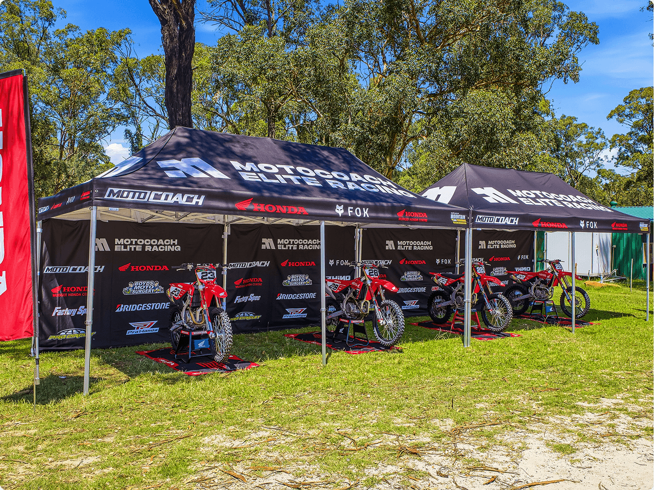 Motocoach Elite Racing pit tents with sponsor branding and the team's Honda race bikes