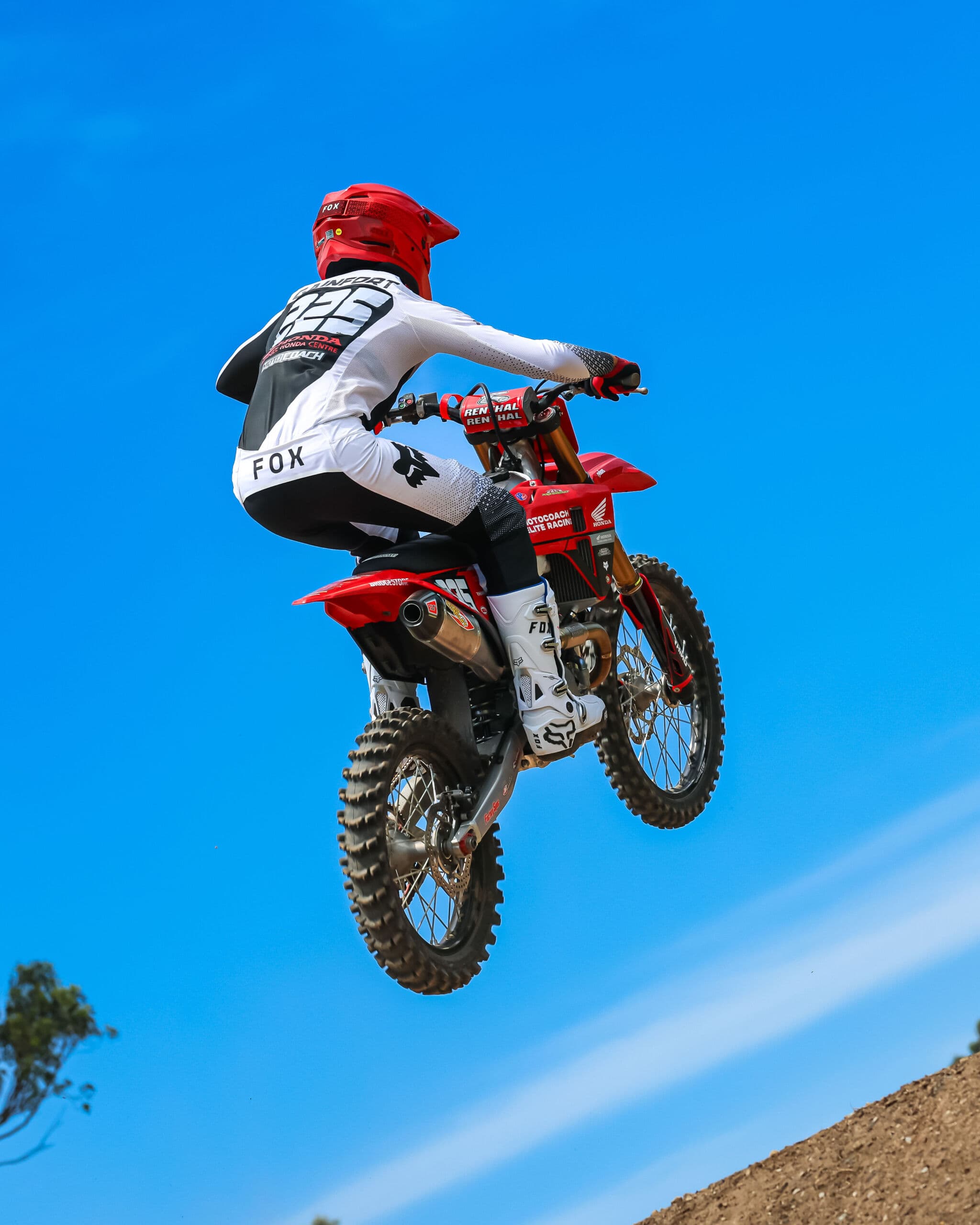 Motocoach Elite Racing rider jumping a Honda motocross bike against a clear blue sky