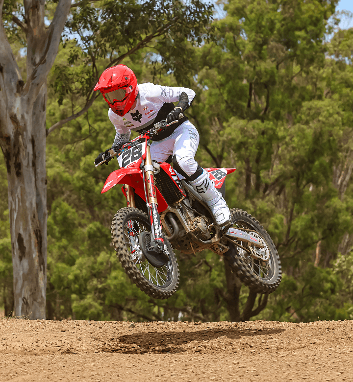 Motocoach Elite Racing rider jumping a Honda motocross bike between gum trees