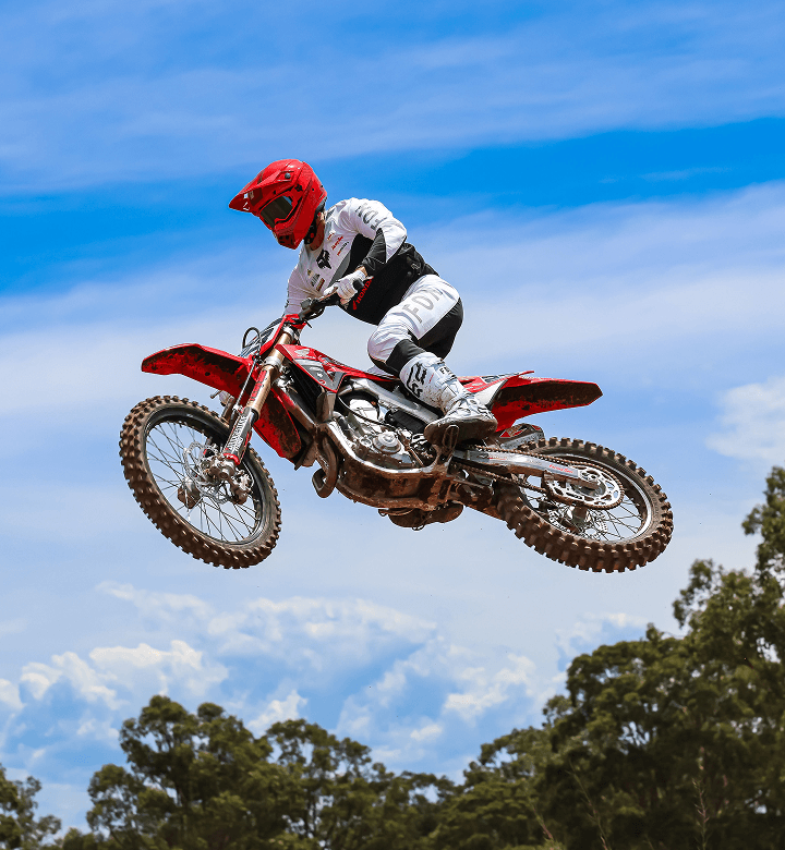 Motocoach Elite Racing rider whipping a Honda motocross bike against a blue sky