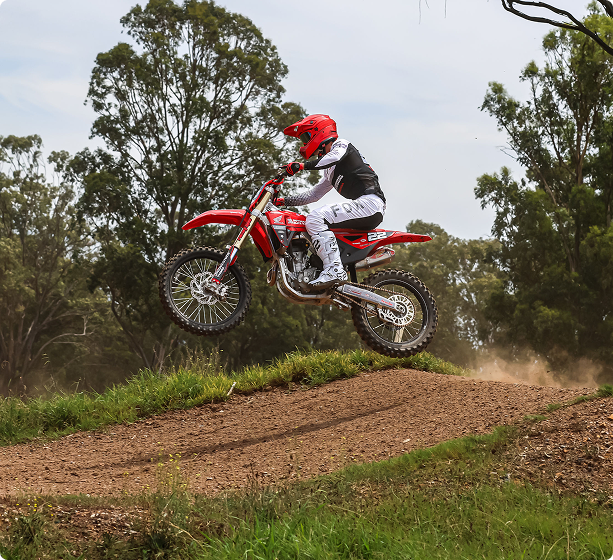 Motocoach Elite Racing rider jumping a Honda motocross bike off a dirt track lip