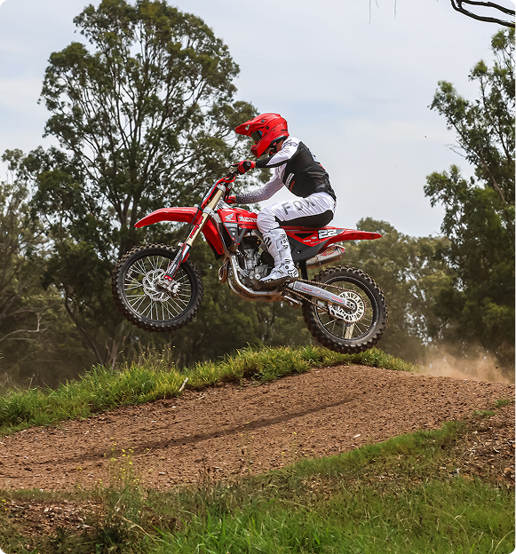 Motocoach Elite Racing rider jumping a Honda motocross bike off a dirt lip in the bush
